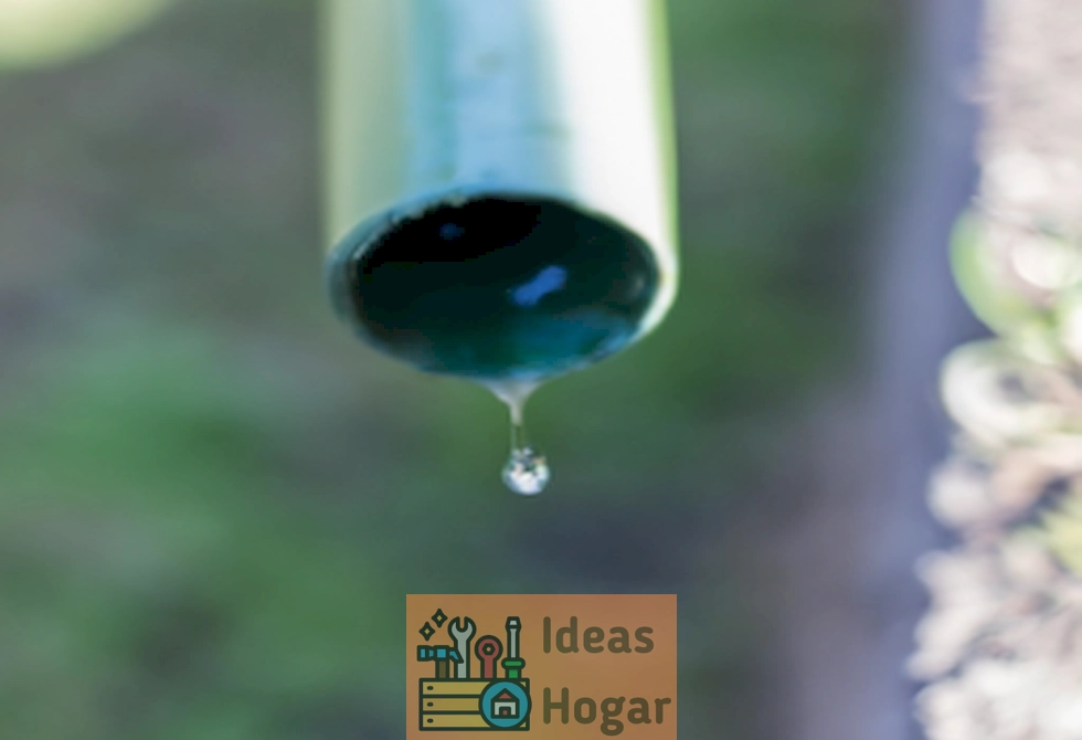Imagen de una tubería con gotas de agua goteando en el jardín, representando una fuga de agua exterior que requiere ser detectada y reparada.