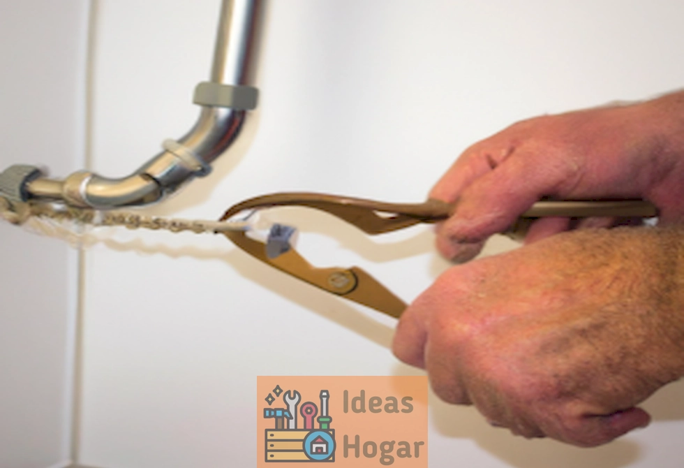 Manos sujetando una llave inglesa y un trapo mientras arreglan una tubería con fuga en una cocina.